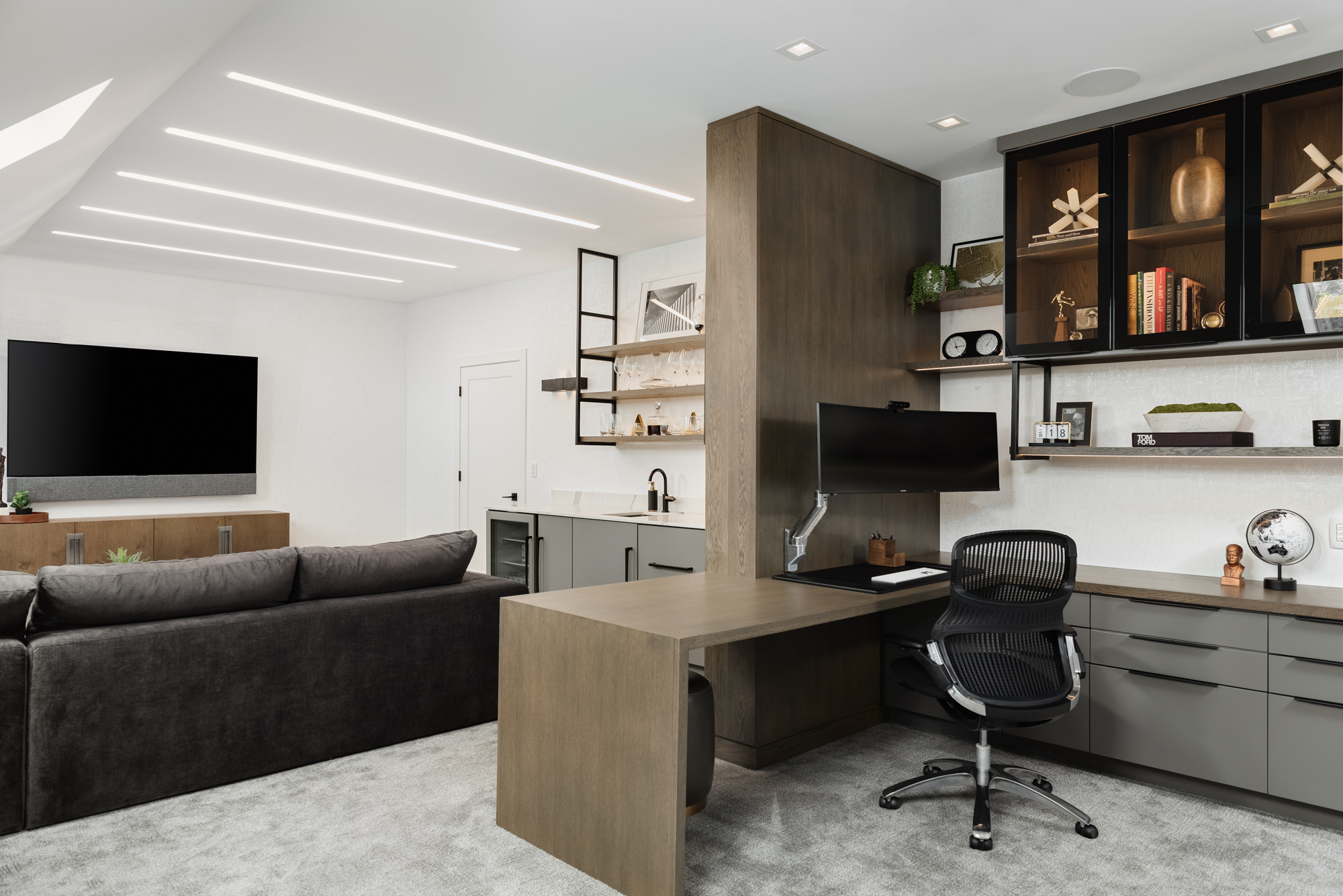 Masculine home office design in attic. Gray modern cabinets, wood desk, white walls, Herman Miller office chair. Attic living room with gray sectional sofa, floating media console, and tv. Interior Design by LC Interiors, best interior designer in Naperville, Illinois.