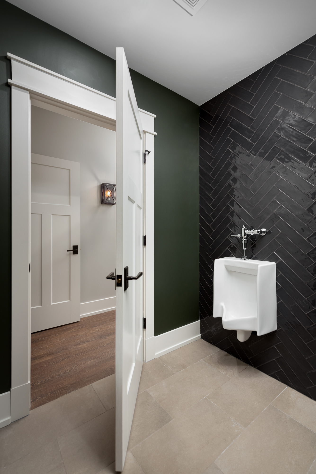 Urinal in basement powder room with black herringbone wall tile and green walls. Designed by LC Interiors in Naperville, IL.